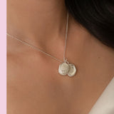 Silver necklace with two round pendants on a person against a pink background