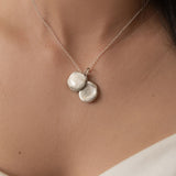 Silver necklace with two round pendants on a person's neck