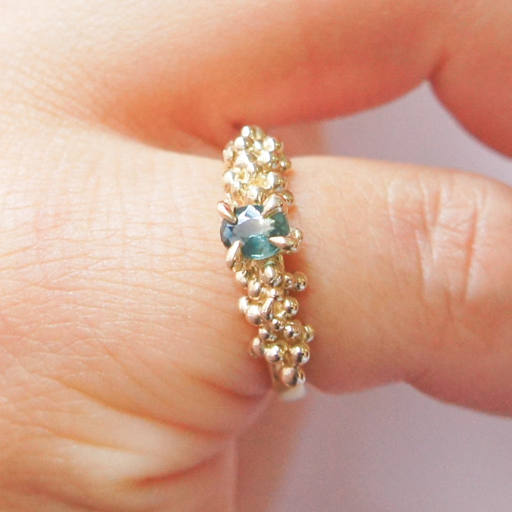 Gold ring with a green gemstone on a finger