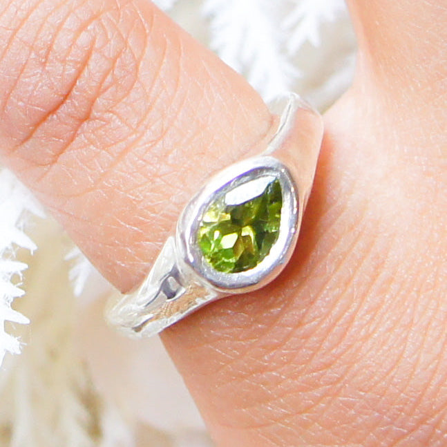 Silver ring with a green gemstone on a finger against a white background