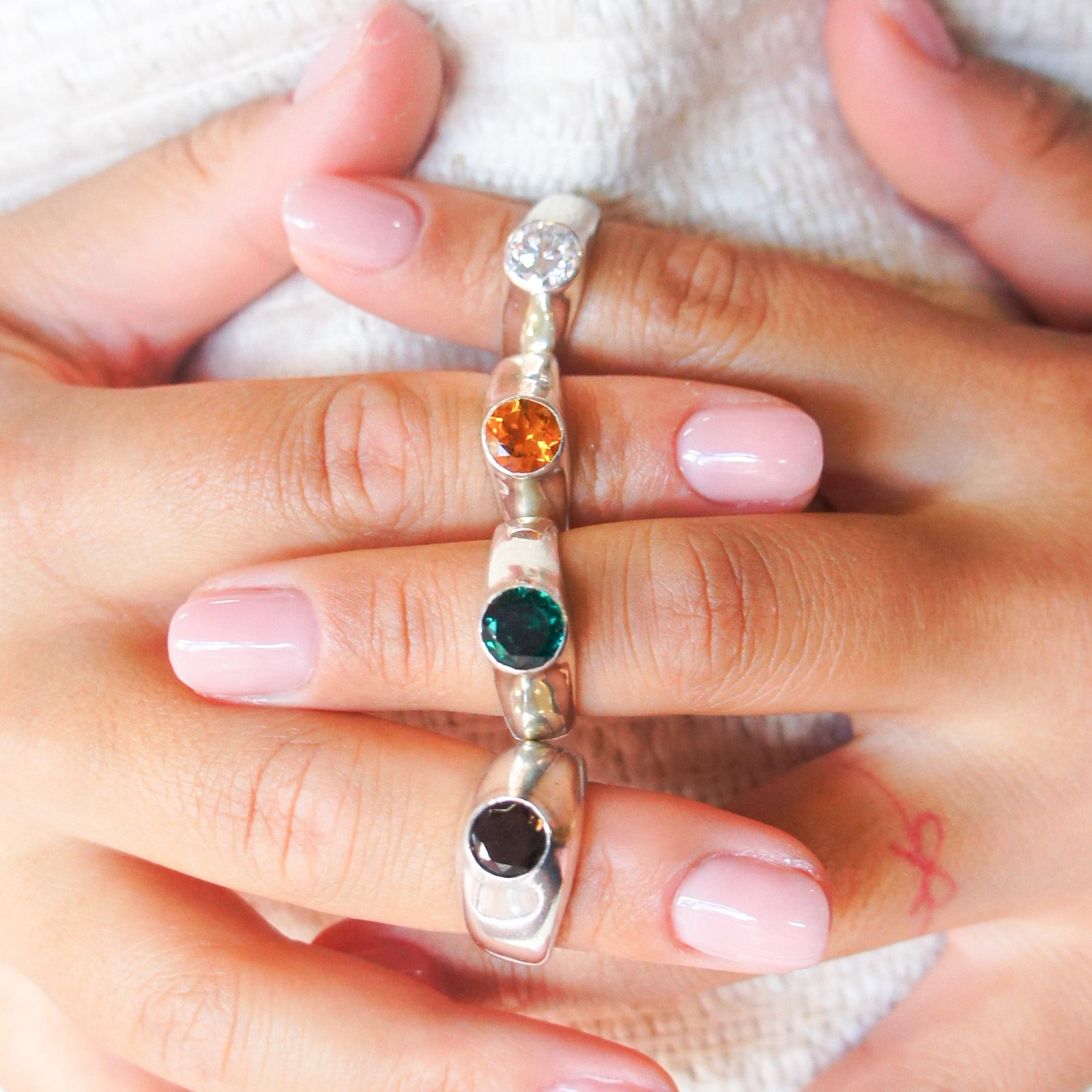 Close-up of a hand wearing a silver signet rings with coloured gemstones on a white background