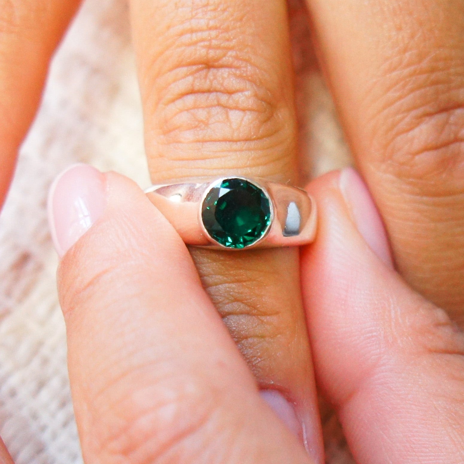 Close-up of a hand wearing a silver ring with a green gemstone.