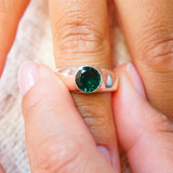 Close-up of a hand wearing a silver ring with a green gemstone.