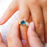 Close-up of a hand wearing a ring with a green gemstone on a light background