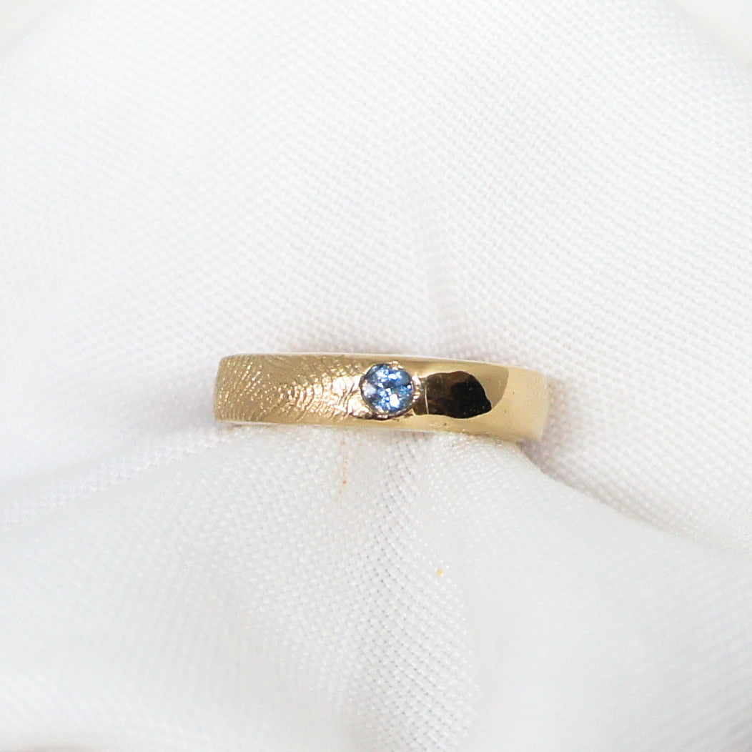 Gold ring with a blue gemstone on a white fabric background
