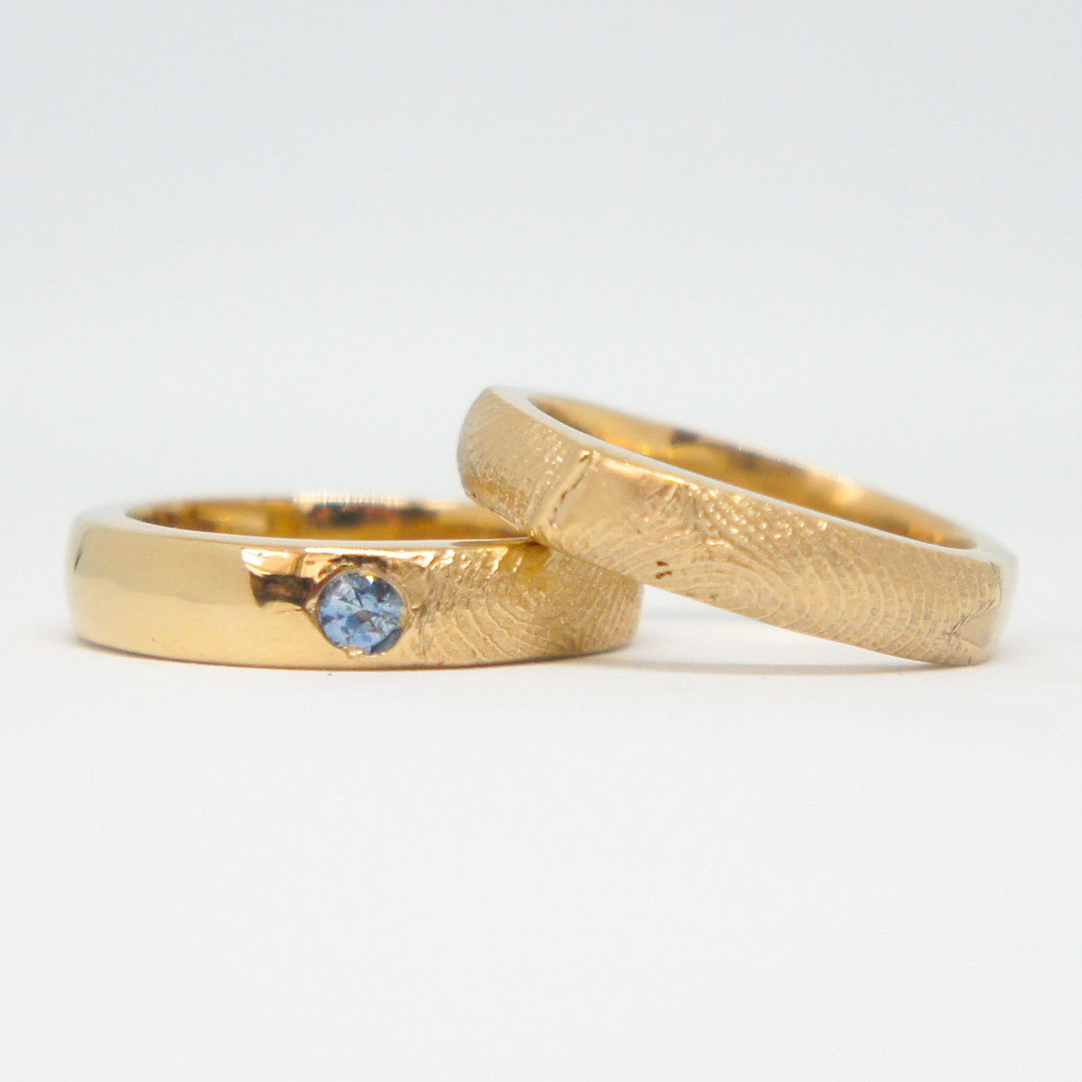 Two gold rings with a blue gemstone on a white background