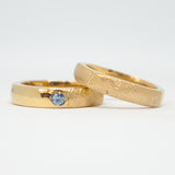 Two gold rings with a blue gemstone on a white background