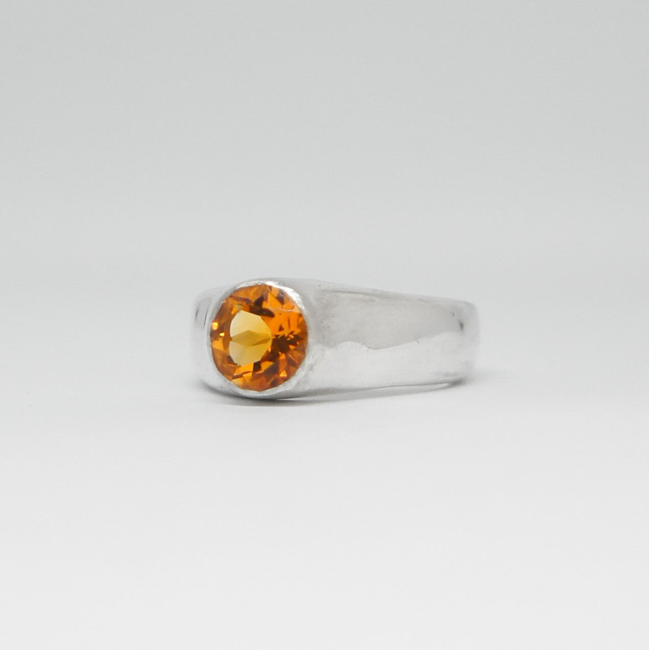 Silver ring with a yellow gemstone on a light gray background