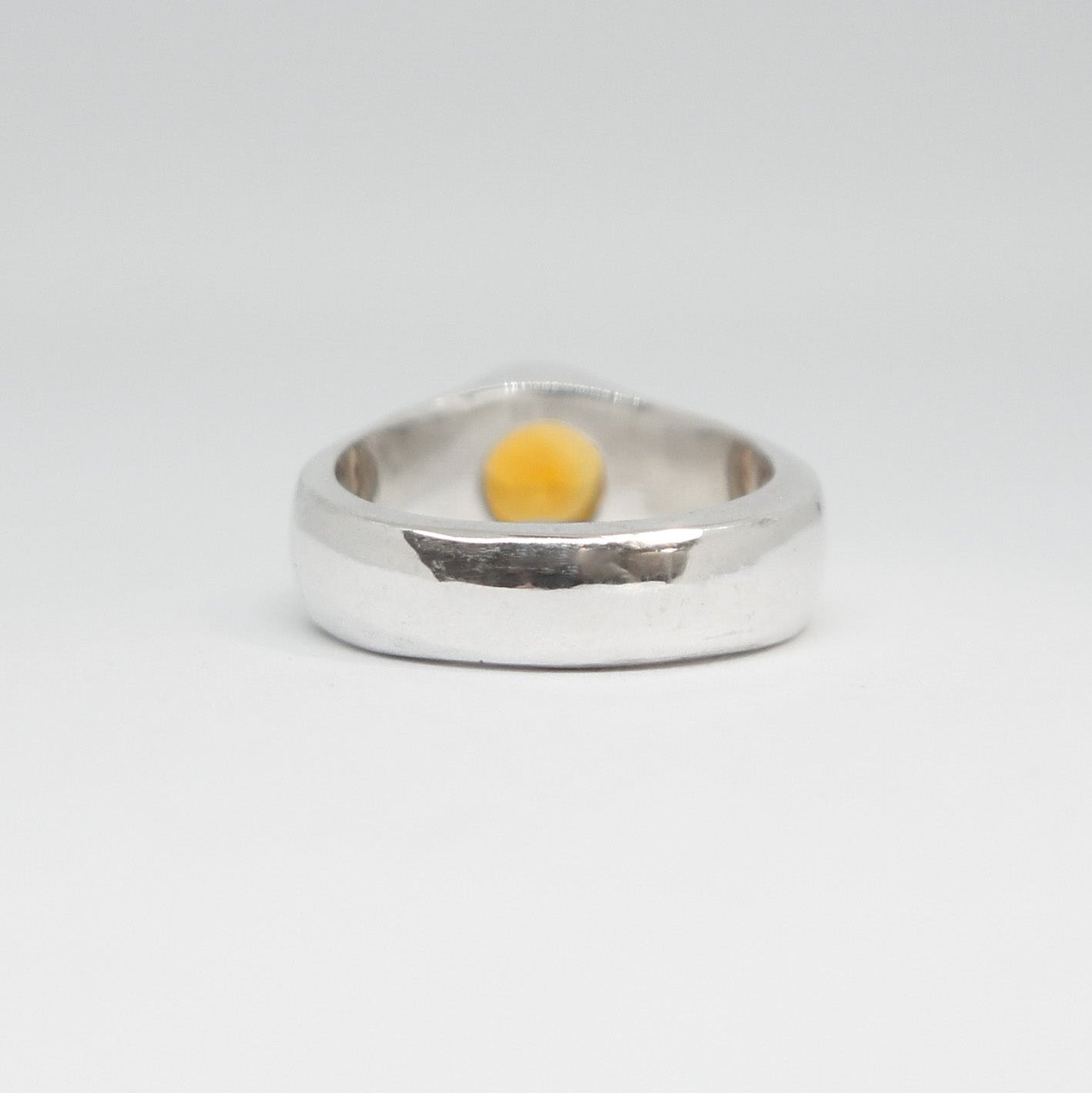 Silver ring with a yellow stone on a white background