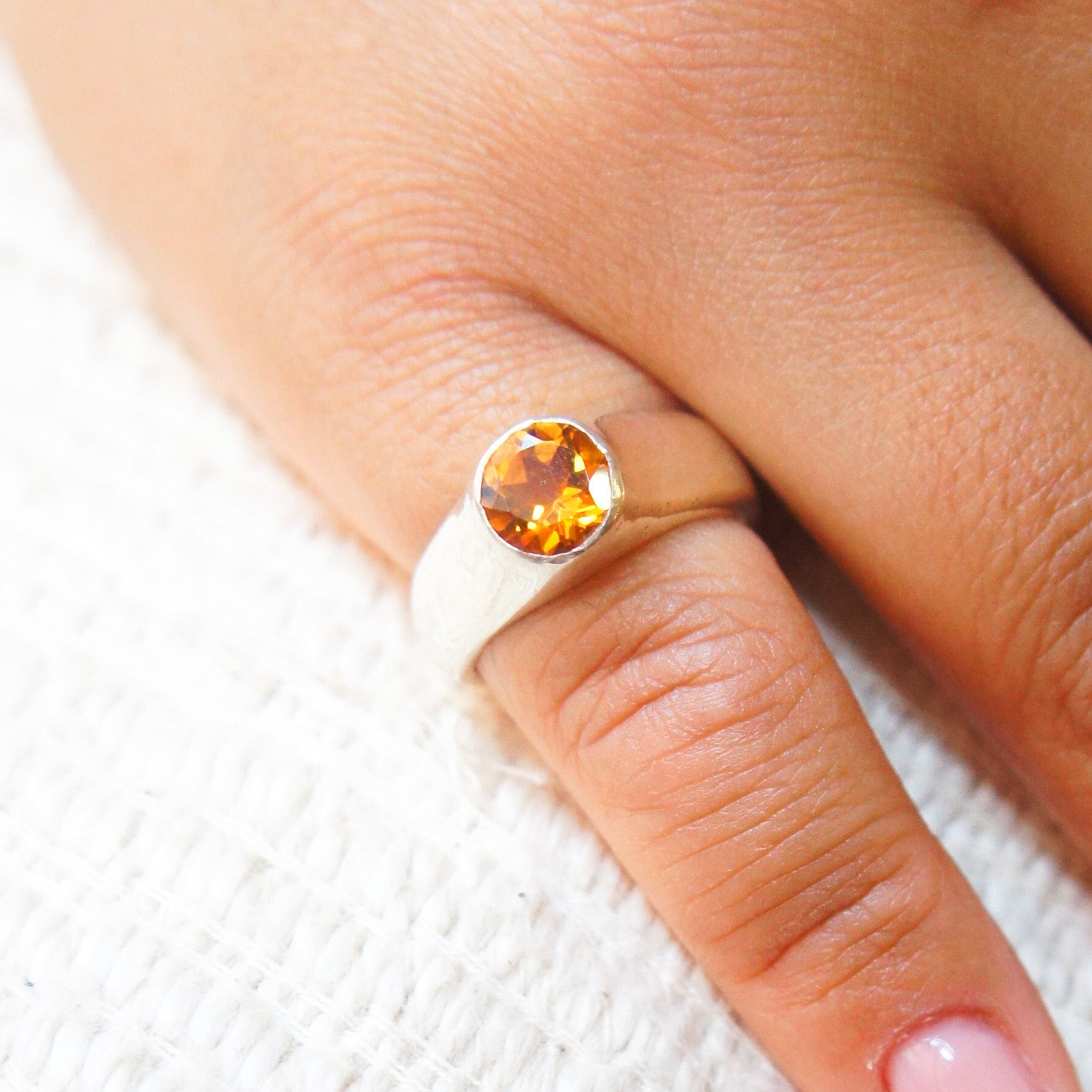 Silver ring with a orange gemstone on a finger 