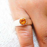 Close-up of a hand wearing a ring with a yellow gemstone on a white fabric background