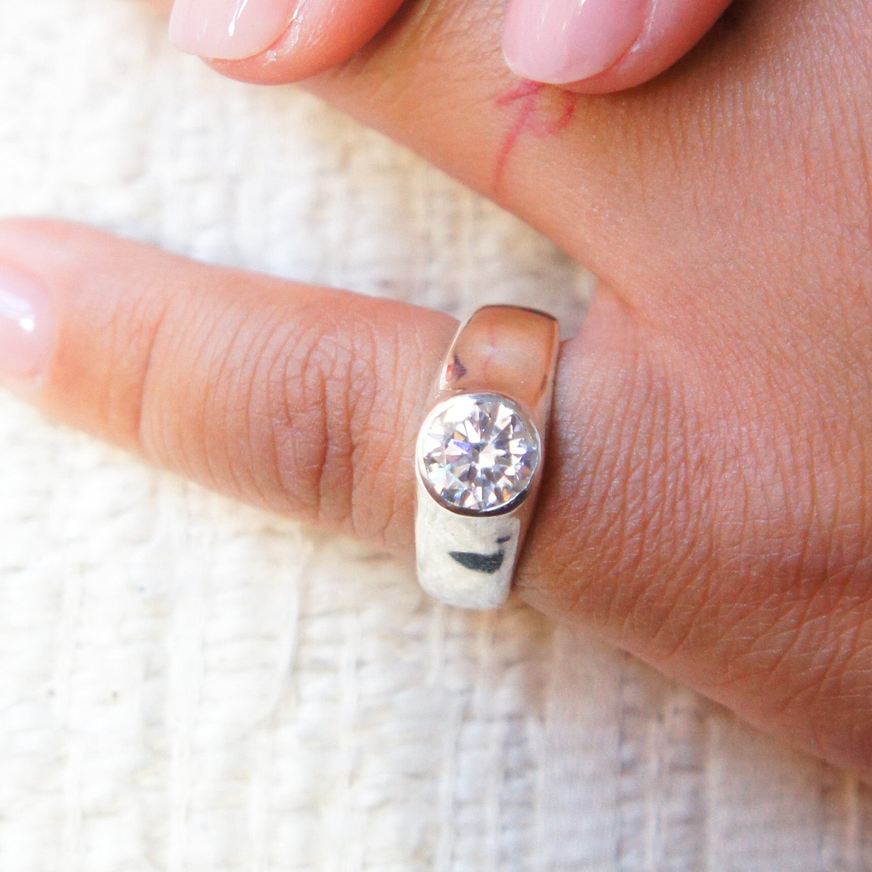 Close-up of a hand wearing a silver ring with a diamond on a white textured background