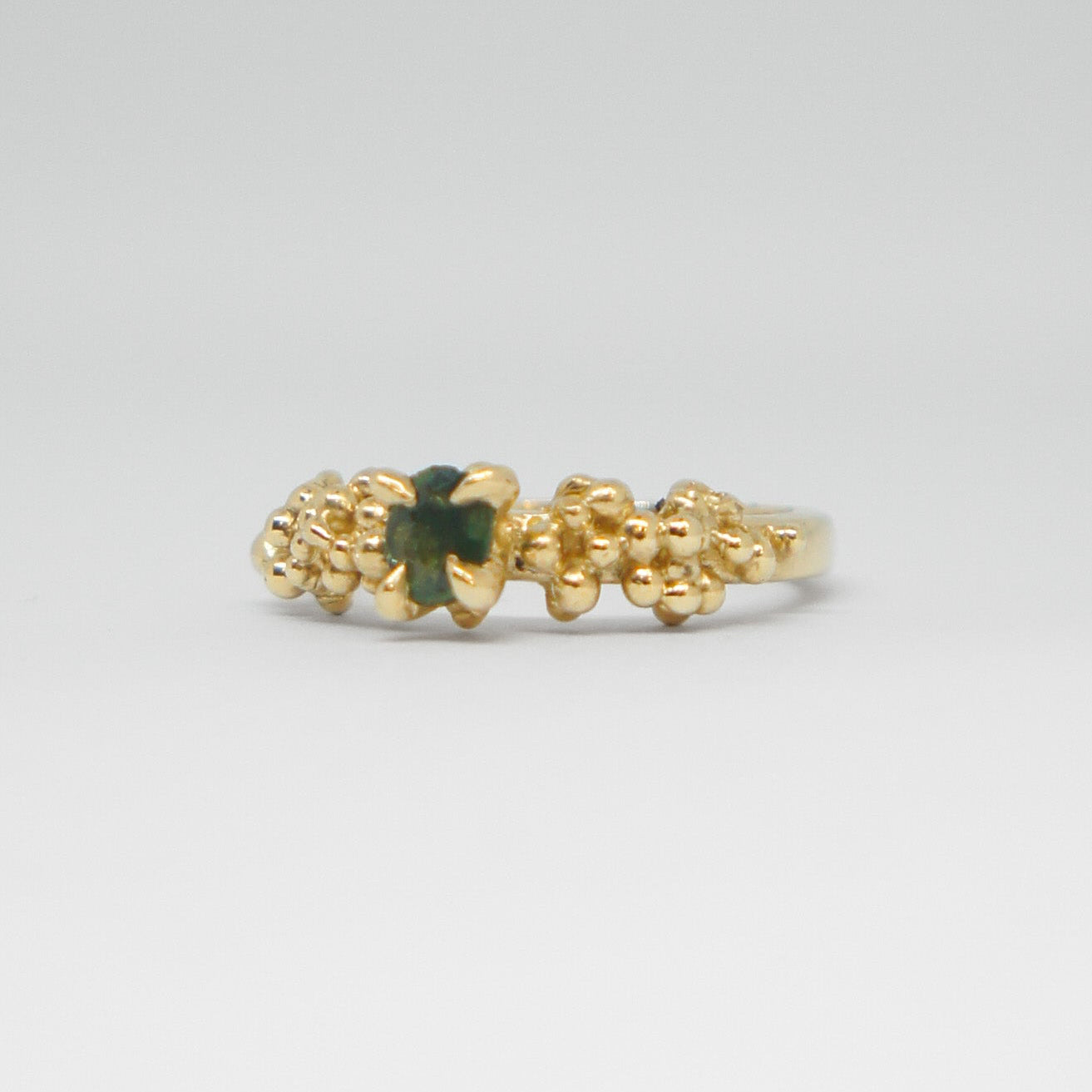 Gold ring with a green gemstone on a light gray background