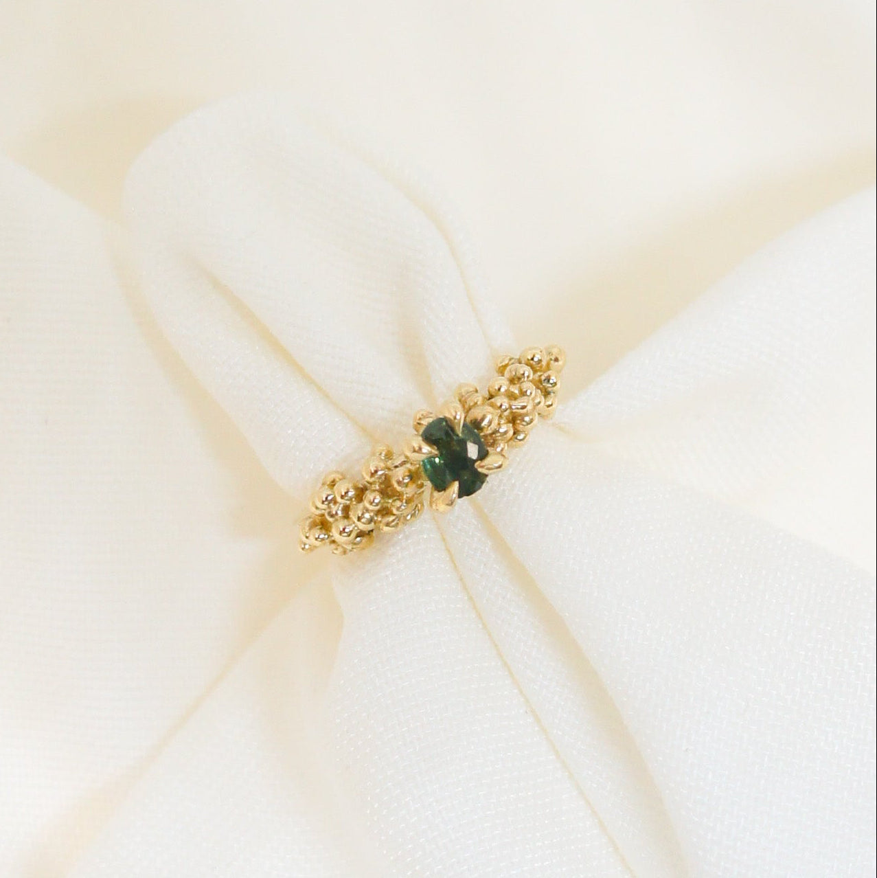 Gold organic ring with a green stone on a white fabric background