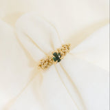 Gold organic ring with a green stone on a white fabric background