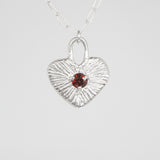 Silver heart-shaped pendant with a red gemstone on a white background
