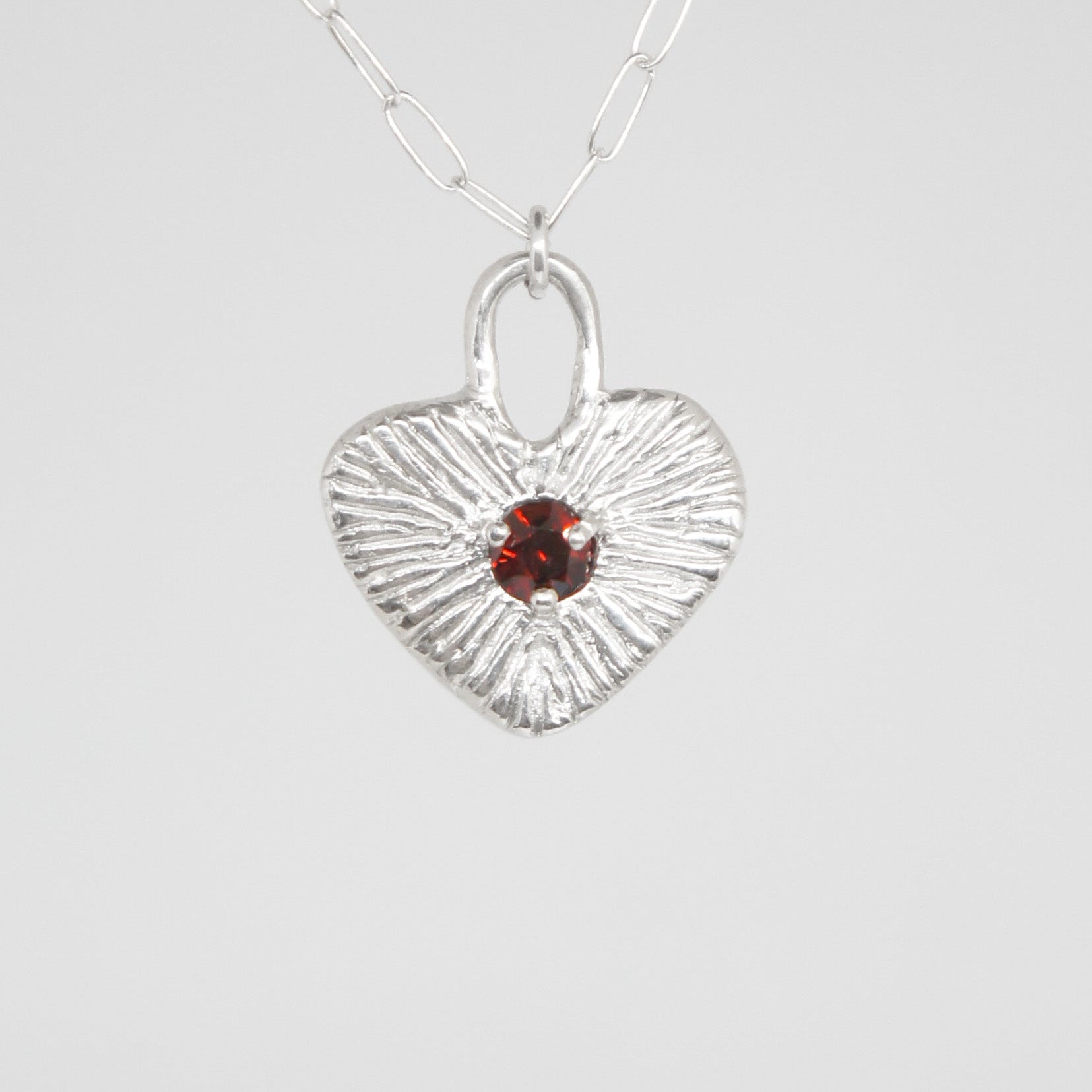 Silver heart-shaped pendant with a red gemstone on a white background