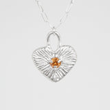 Silver heart-shaped pendant with a small orange gemstone on a white background