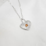 Silver necklace with a heart-shaped pendant featuring a small orange gemstone on a white background