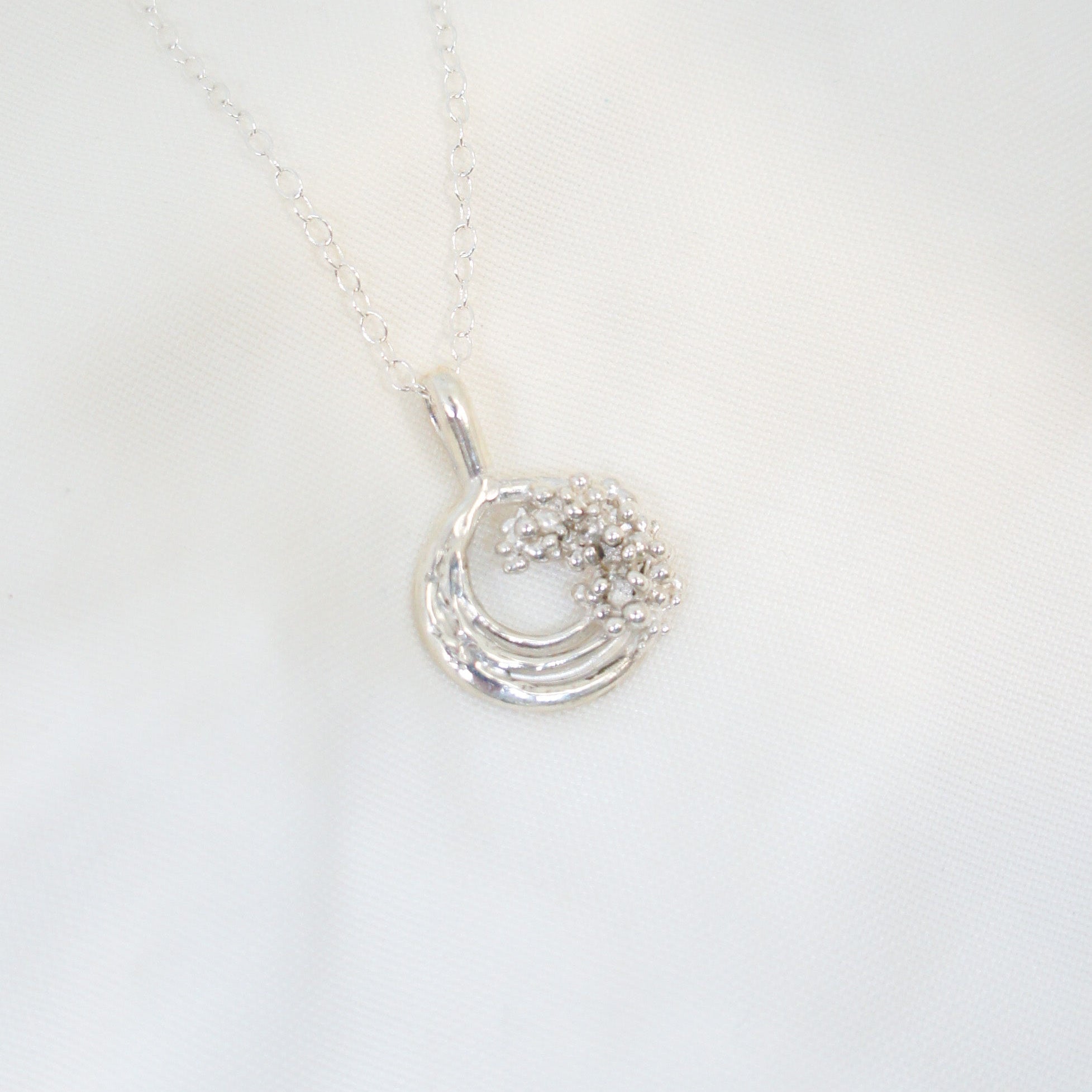 Silver necklace with a circular pendant on a white background