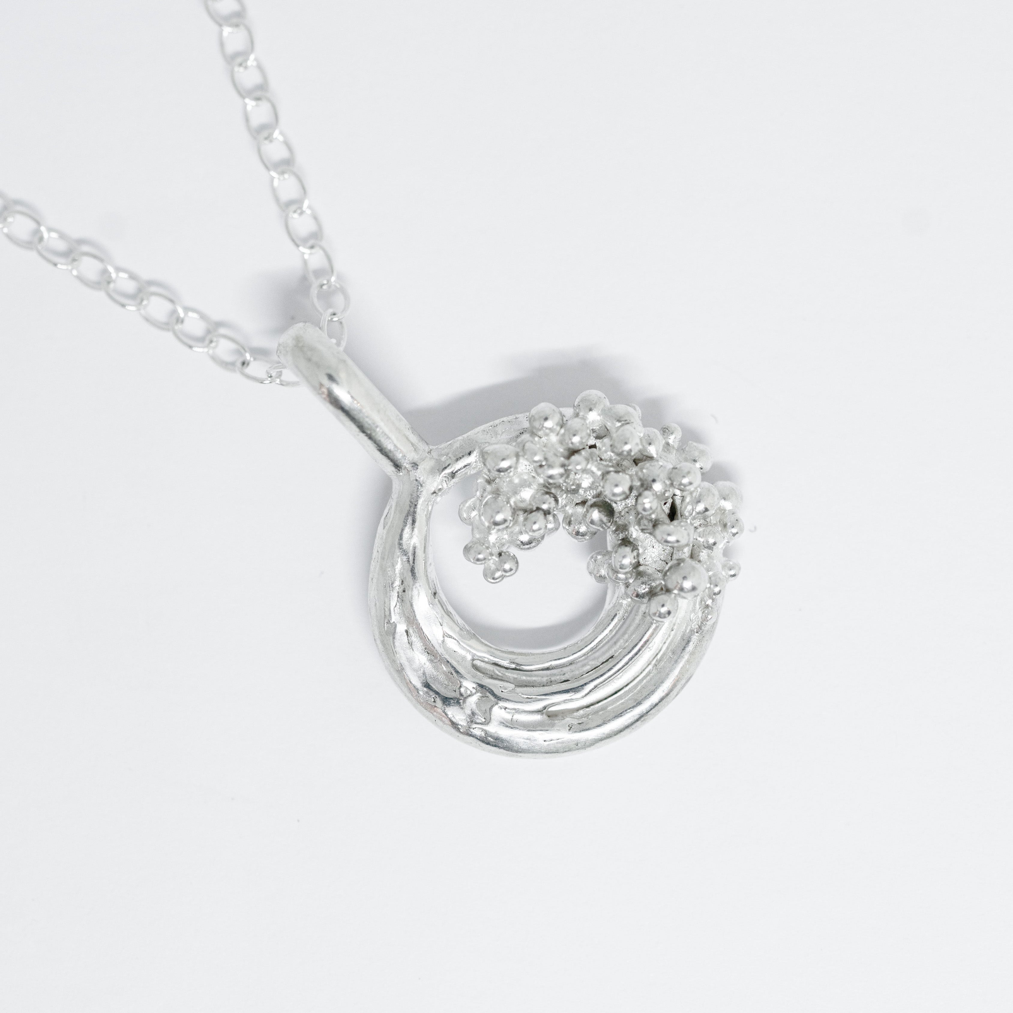 Silver necklace with a circular pendant on a white background