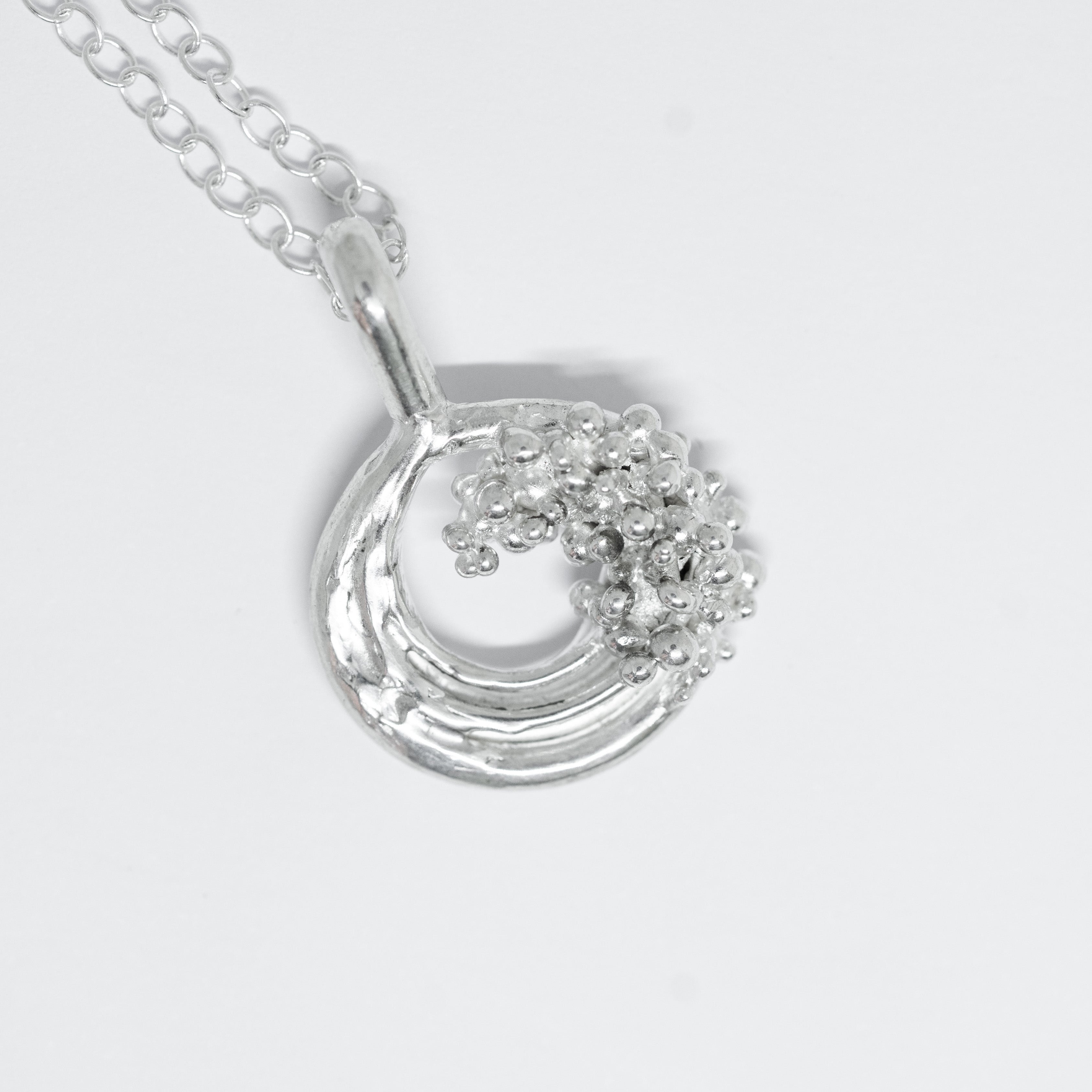 Silver necklace with a wave-shaped pendant on a light gray background