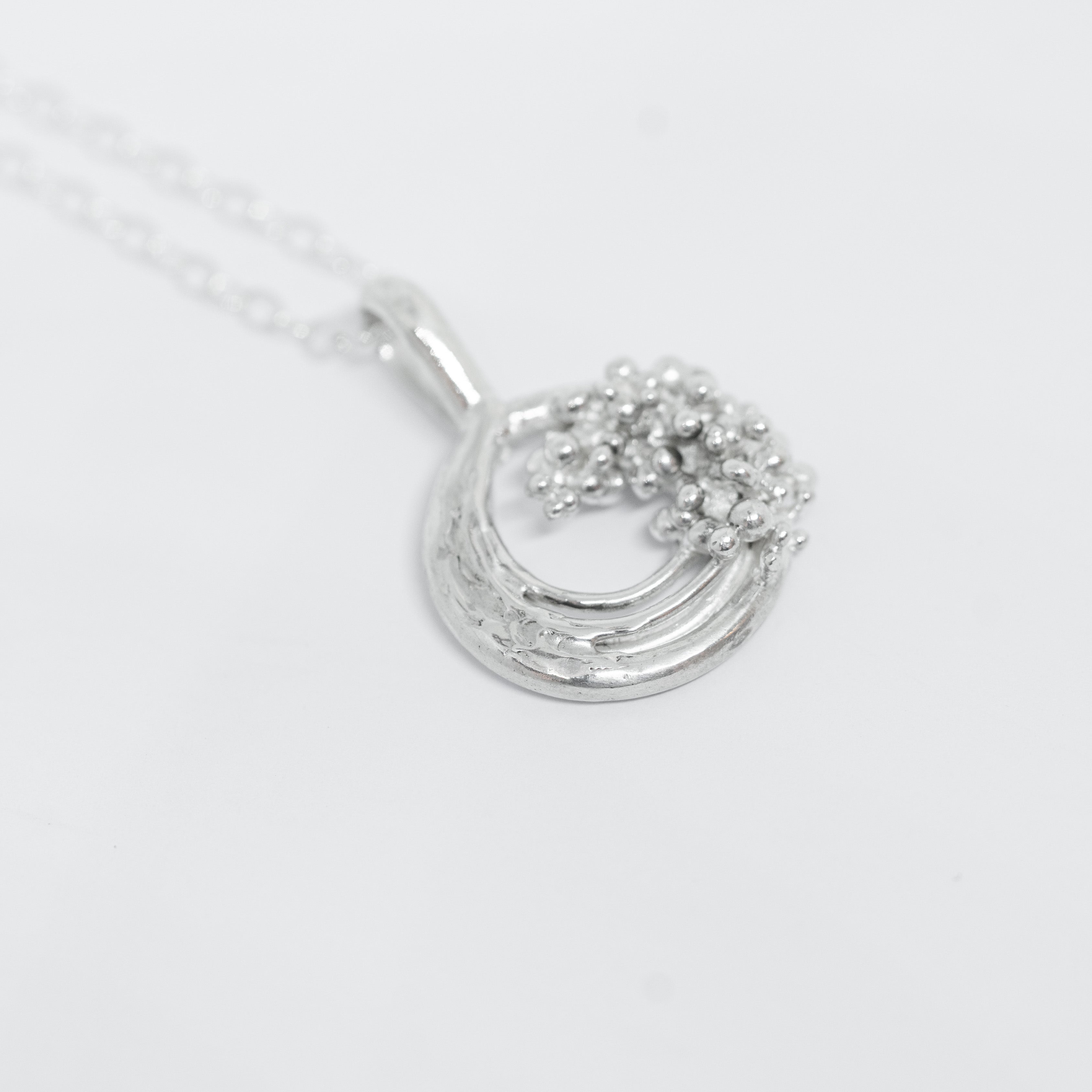 Silver necklace with a circular pendant on a white background