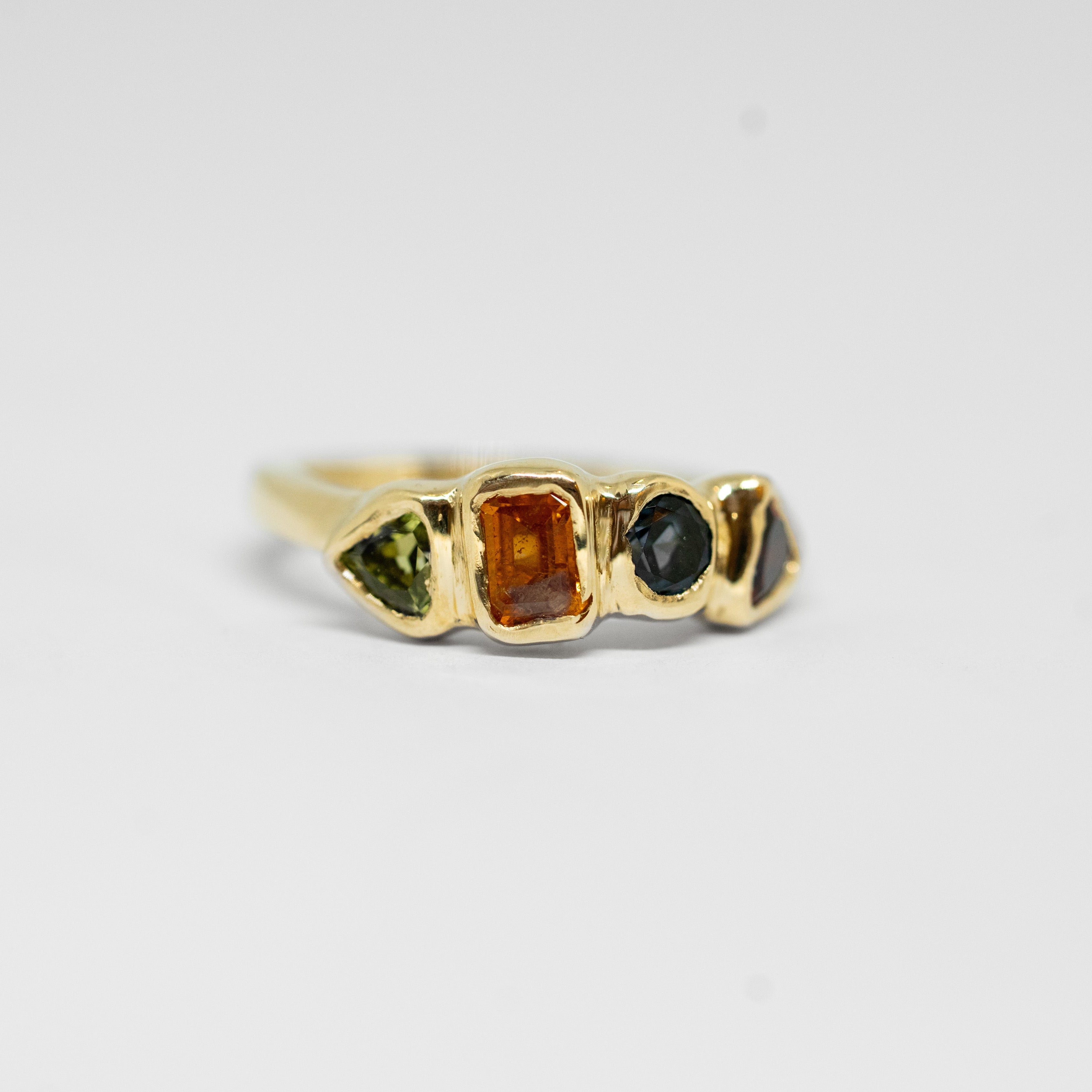 Gold ring with four coloured gemstones on a white background