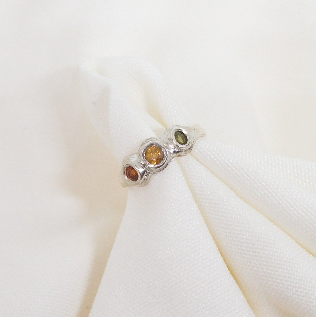 Silver ring with colored stones on a white fabric background