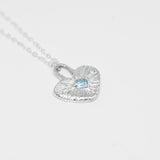 Silver heart-shaped necklace with a blue gemstone on a light gray background