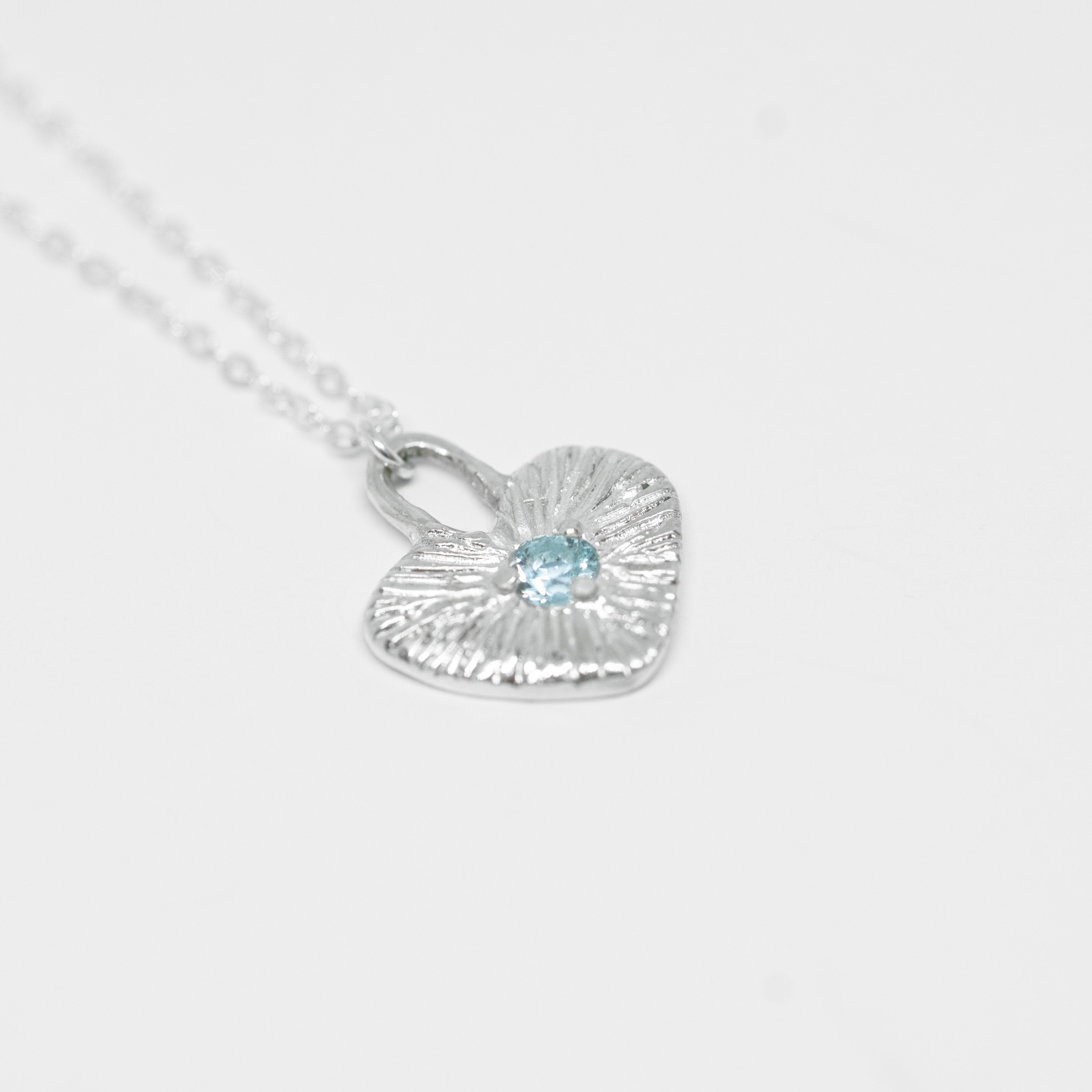 Silver heart-shaped necklace with a blue gemstone on a light gray background