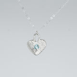 Heart-shaped silver pendant with a blue gemstone on a gray background