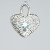 Silver heart-shaped pendant with a central gemstone on a light gray background