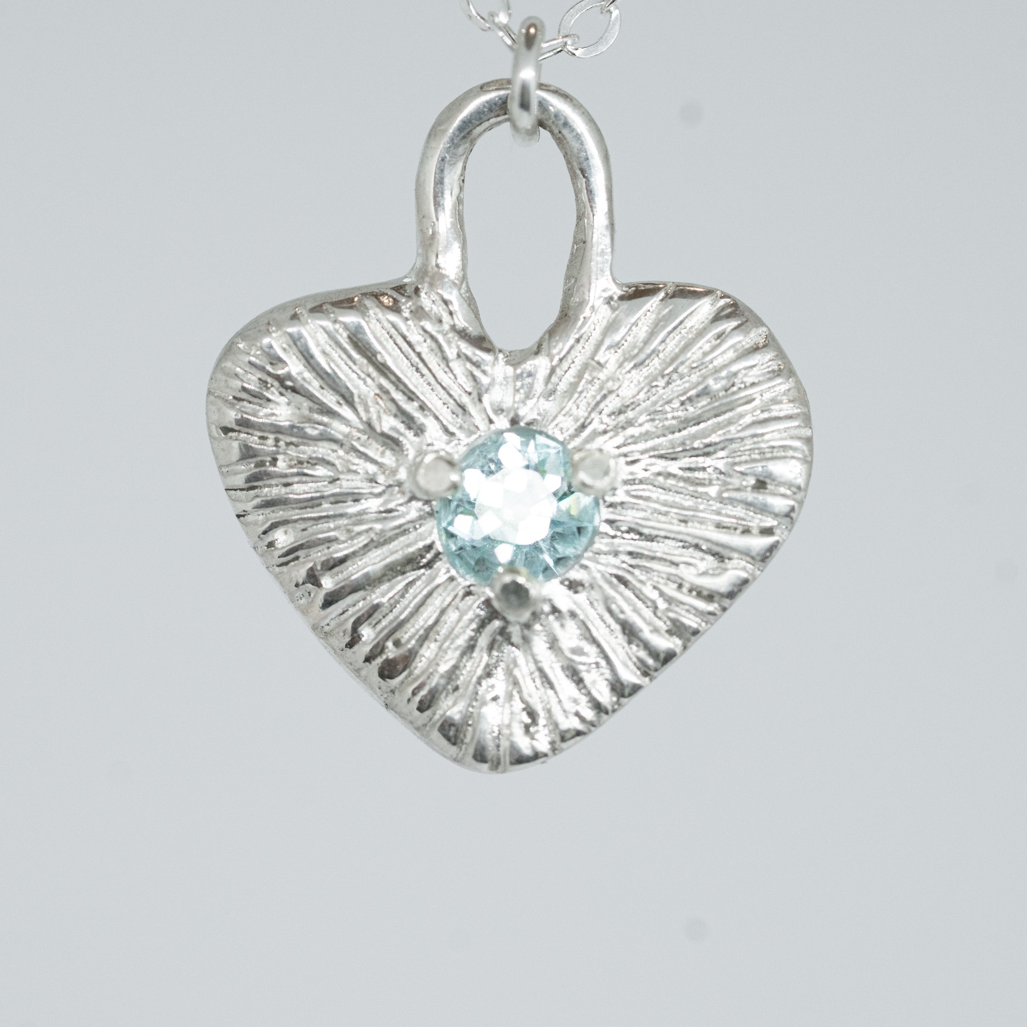Silver heart-shaped pendant with a central gemstone on a light gray background
