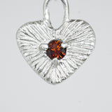 Silver heart-shaped pendant with a red gemstone on a white background