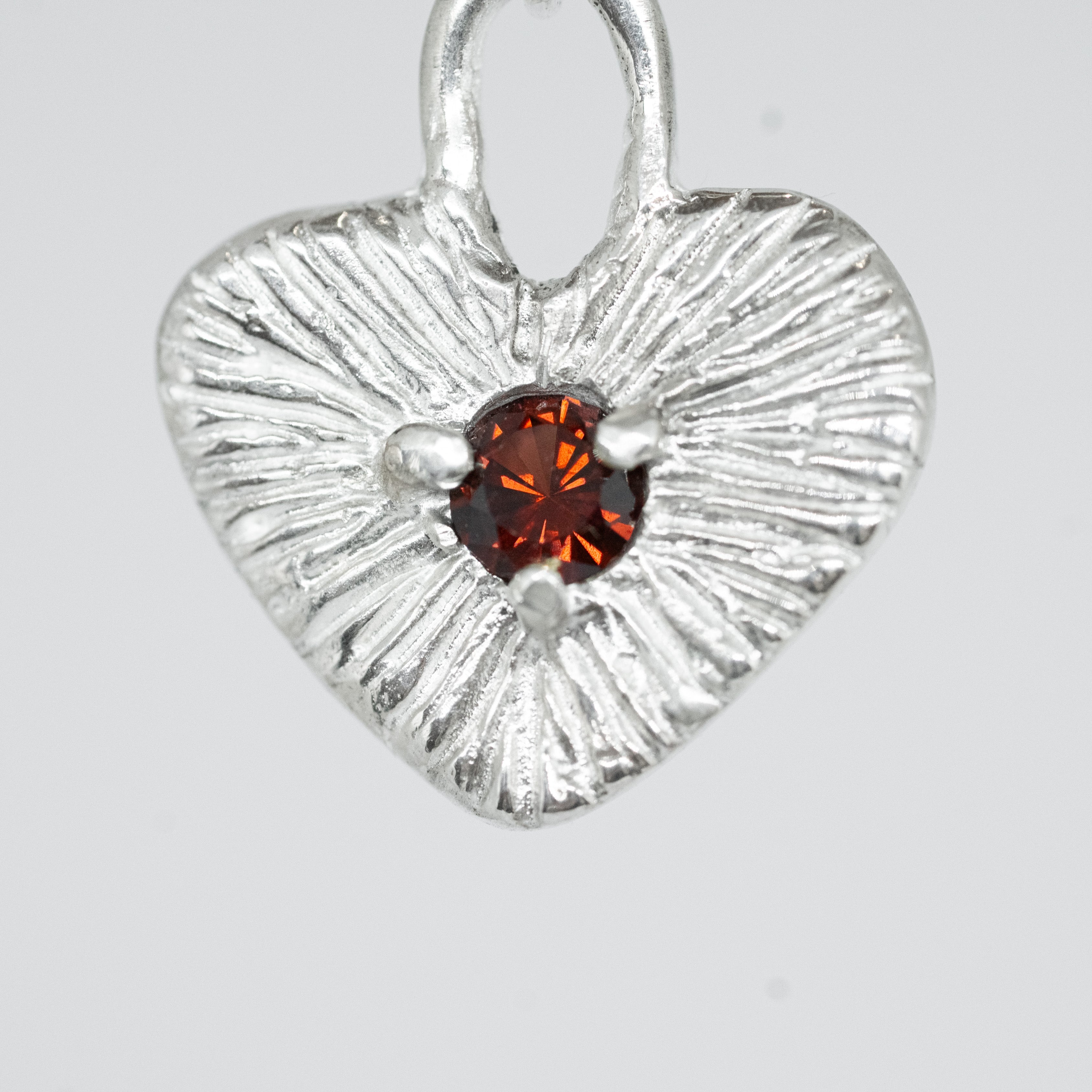Silver heart-shaped pendant with a red gemstone on a white background