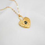 Gold heart-shaped pendant necklace with a black gemstone on a light gray background