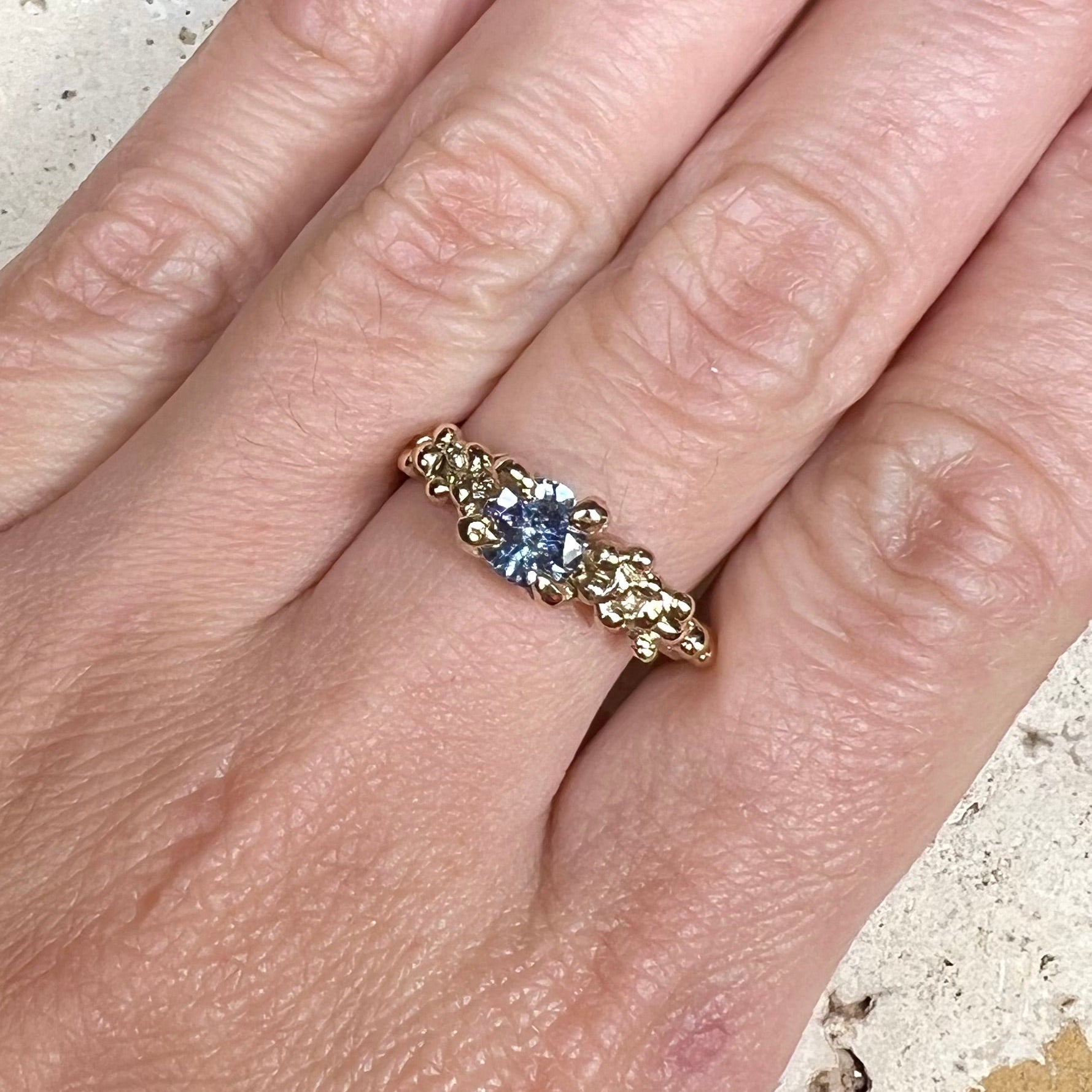 Gold ring with a blue gemstone on a person's finger against a textured background