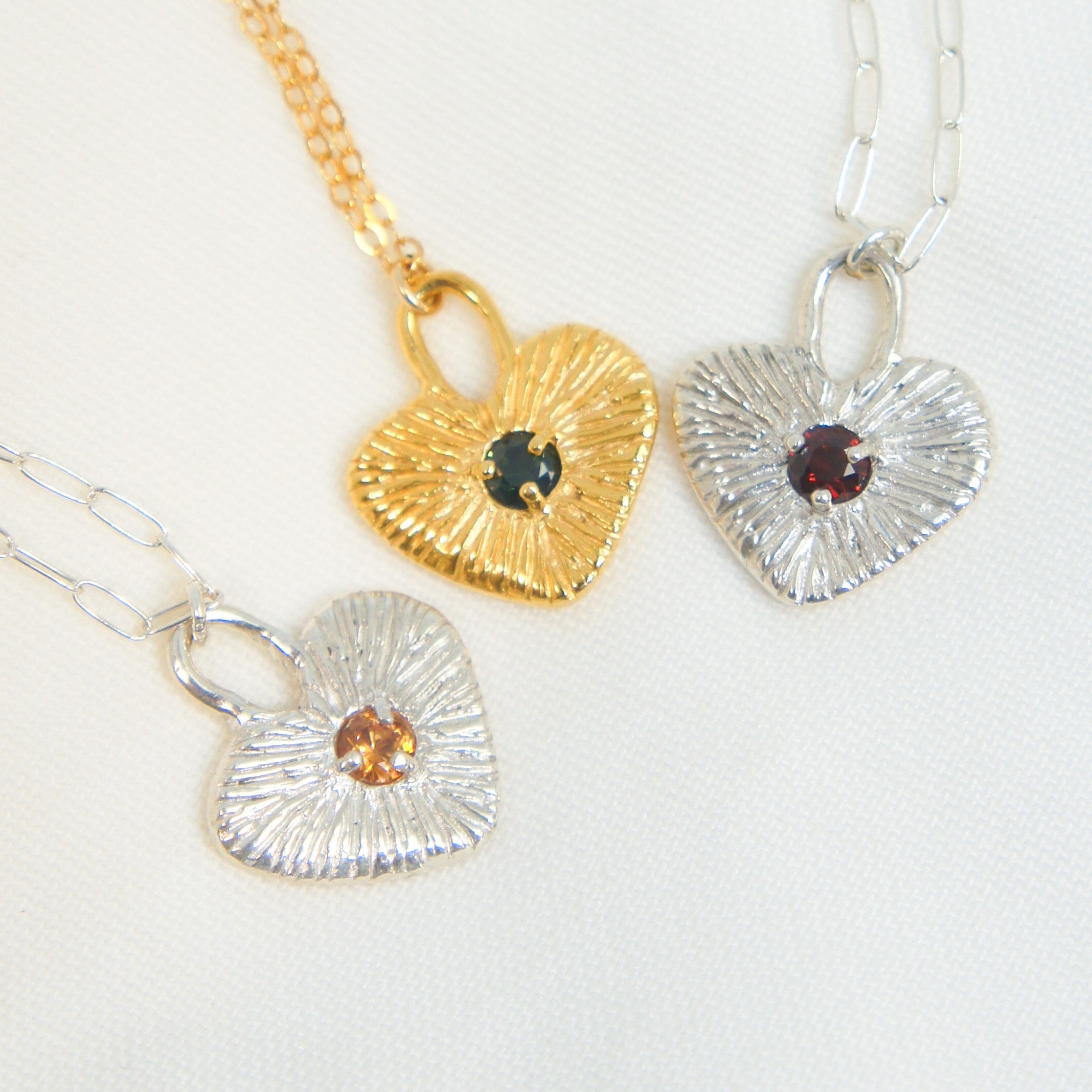 Three heart-shaped pendants on gold, silver, and gold chains against a white background.