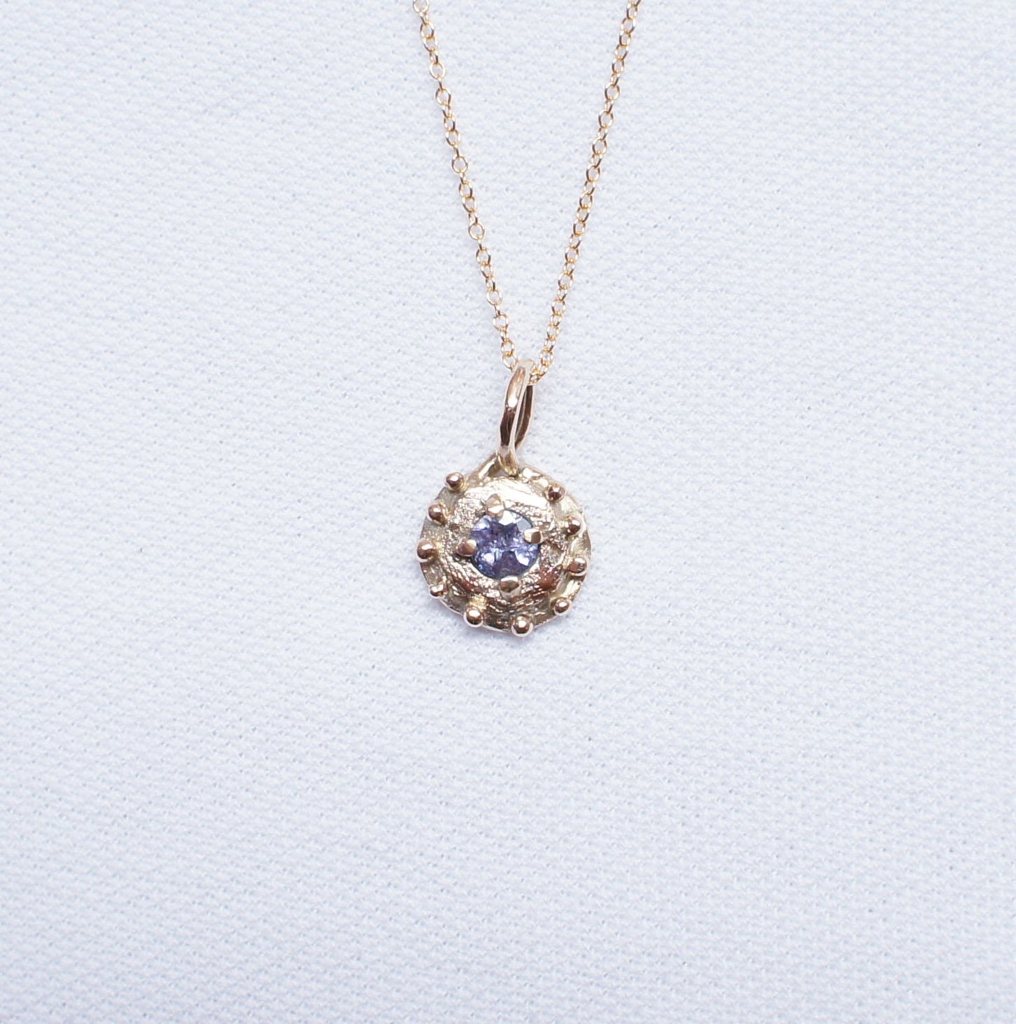 Gold necklace with a organic pendant on a light gray background