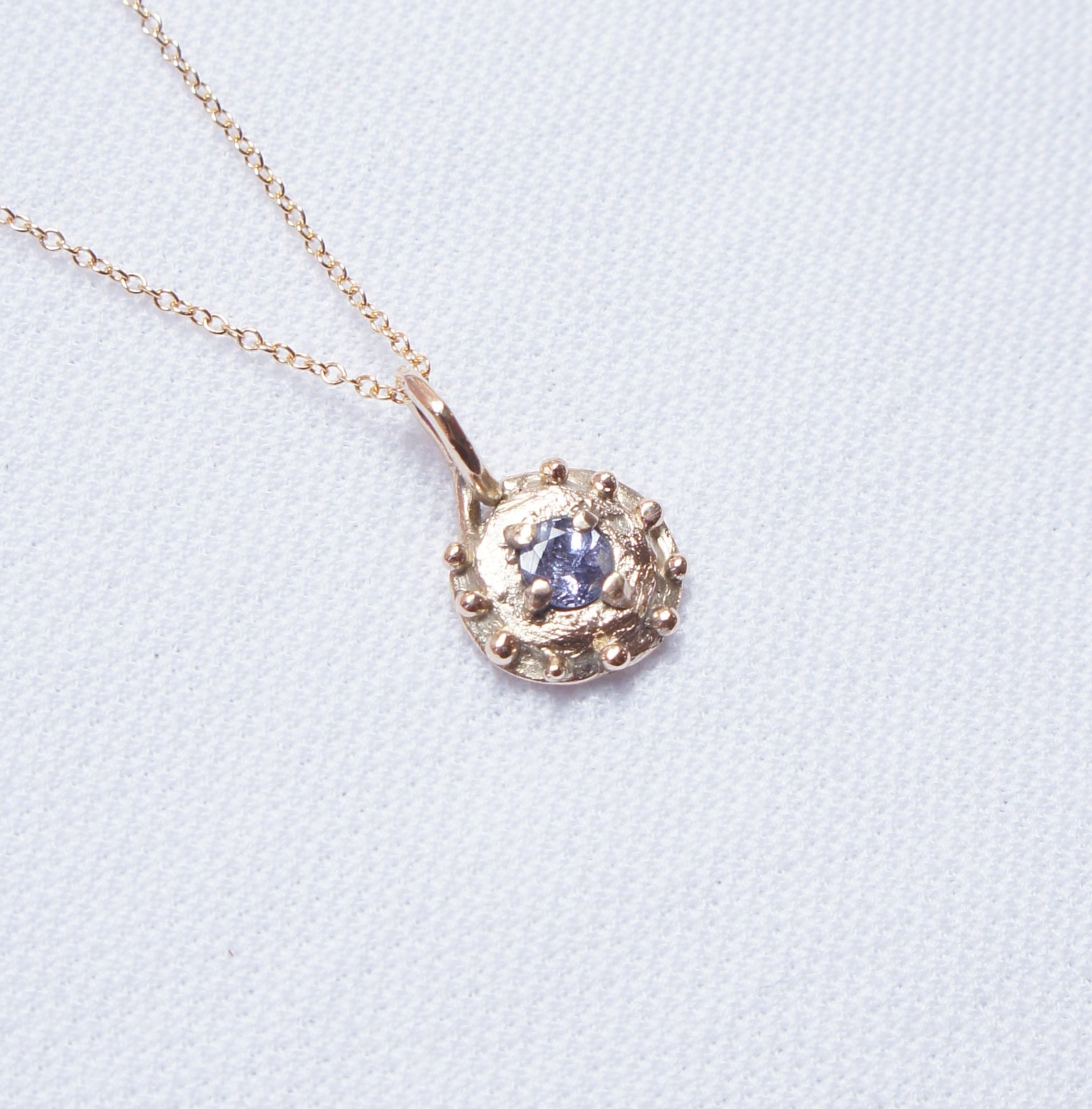 Gold necklace with a round pendant on a light blue background